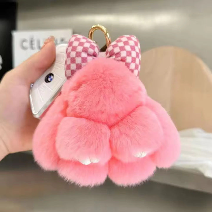 Pink fluffy keychain with a checkered bow held by a hand.