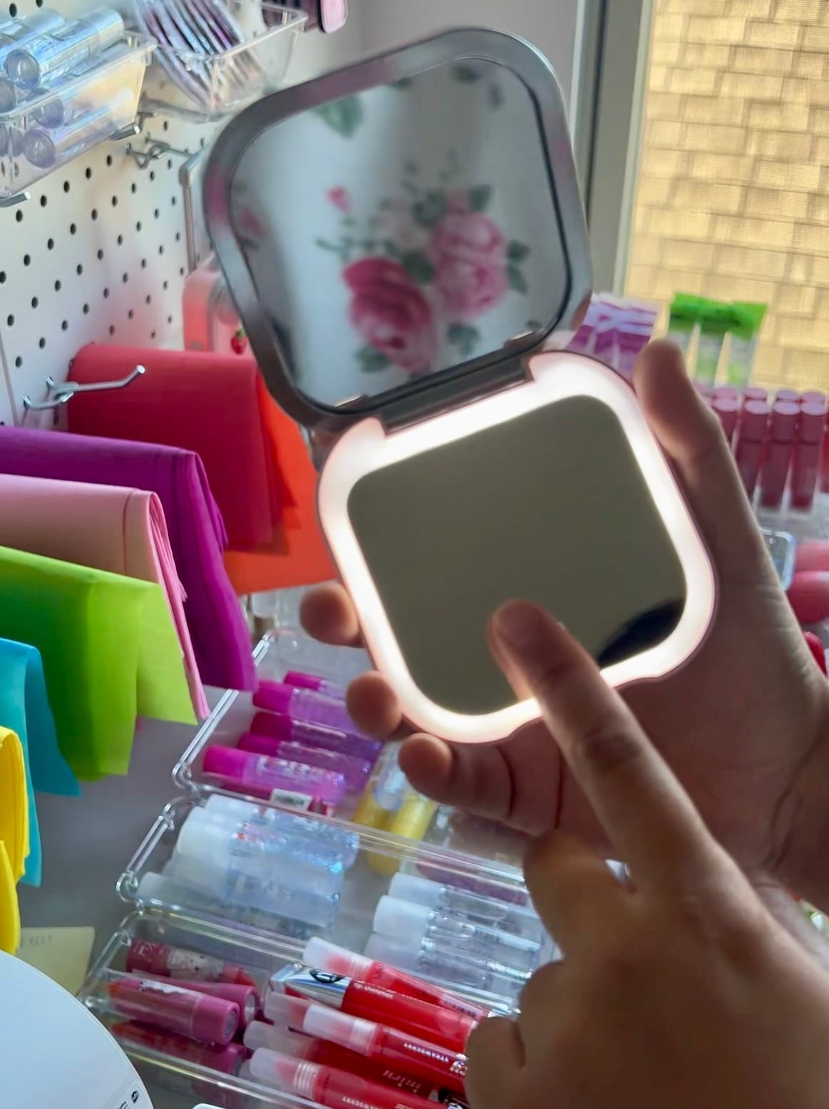 Handheld mirror with LED light held by a person in a store setting.
